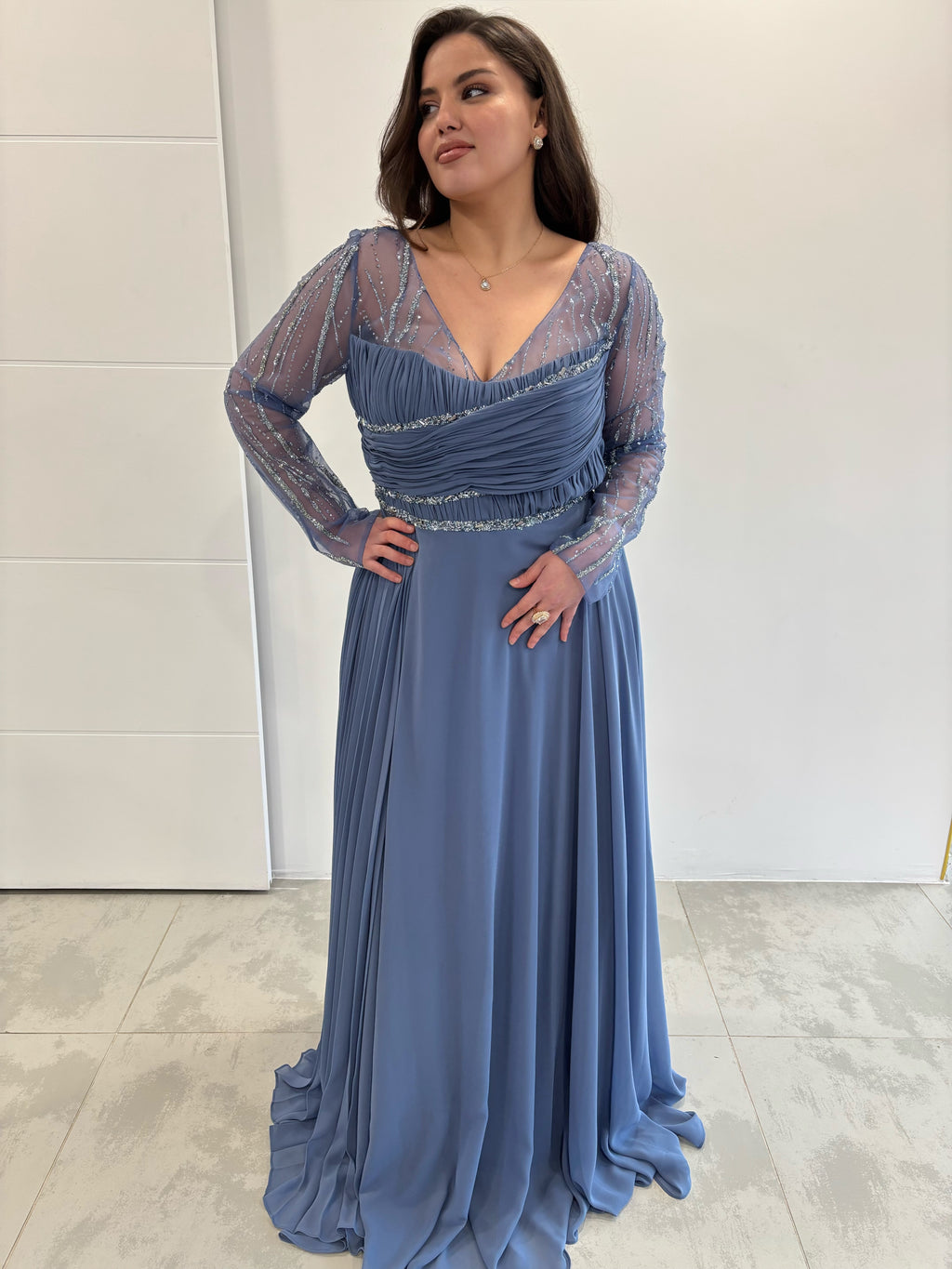 Robe de soirée bleu évasée, col en V et manches longues transparents pailletés, avec traine plissée sur le coté 