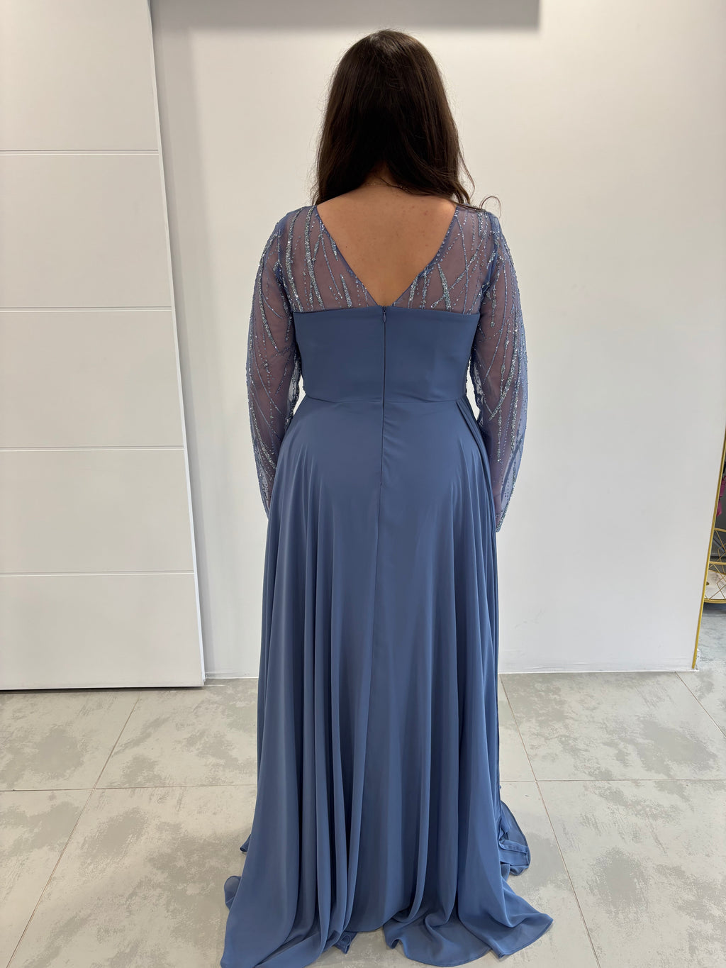 Robe de soirée bleue fluide évasée, dos en v avec fermeture éclaire et manches transparentes pailletées. 