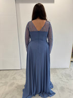 Robe de soirée bleue fluide évasée, dos en v avec fermeture éclaire et manches transparentes pailletées. 