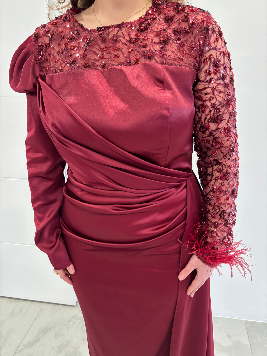 Robe de soirée bordeaux en satin, manches longues dont une manche transparente pailleté avec plumes au poignet, traine sur le coté