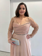 Robe de soirée rose poudrée évasée, manches longues transparentes pailletées, buste et traine sur le coté plissés, vue de près 
