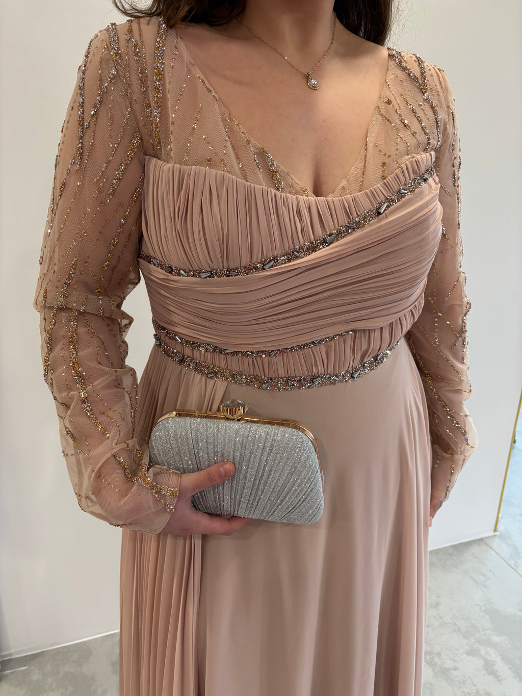Robe de soirée rose poudrée évasée,  vue détaillée sur manches longues transparentes pailletées, buste et traine sur le coté plissés 
